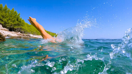 LOW ANGLE VIEW: Female legs caught in air before plunging into crystal blue sea. Crystal clear...