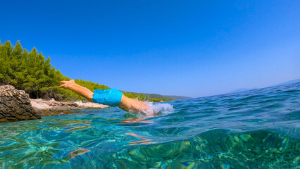 LOW ANGLE VIEW: Male legs caught in the air before plunging into crystal blue sea. Refreshing dive...