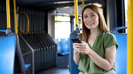 Happy redhead woman using smartphone in a city bus