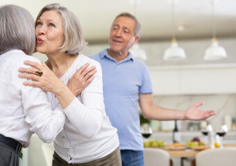 Obraz premium Two elderly woman greet each other by kissing each other on the cheek. While the men shake hands