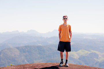 Portrait of a Brazilian man wearing a yellow T-shirt and sunglasses. He is smiling and looking at the camera. In the background, there is a mountainous landscape