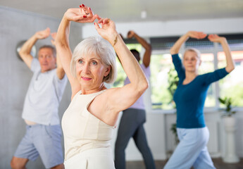 Active senior lady enjoying passionate flamenco dance during group class with adult men and women....