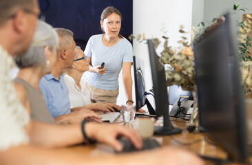 Elderly people listen attentively to female teacher during computer teaching lesson in nursing home