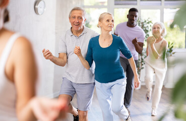 Group of positive adults engaged in dynamic dance in training room during workout session