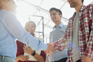 Obraz premium Young startup in casual clothes shaking hands in a modern office space by the window.