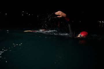 A determined professional triathlete undergoes rigorous night time training in cold waters,...