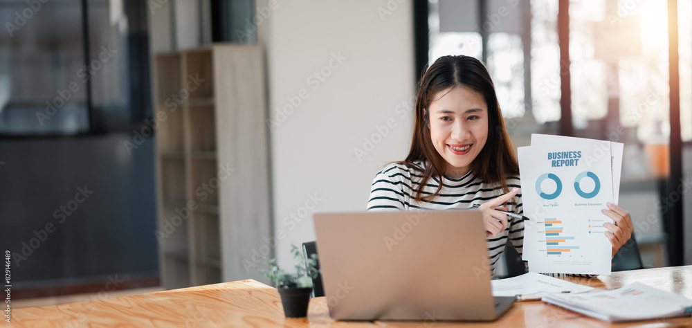 Poster a woman is holding a laptop and pointing to a presentation on a screen. she is smiling and she is ex