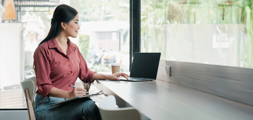 A woman is sitting at a desk with a laptop and a clipboard. She is smiling and she is enjoying her...