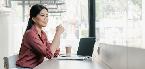 A woman is sitting at a table with a laptop and a cup of coffee. She is smiling and she is enjoying her time