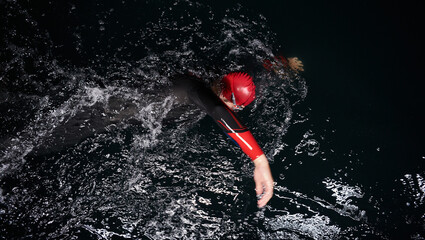 A determined professional triathlete undergoes rigorous night time training in cold waters,...