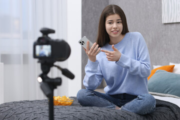 Smiling teenage blogger pointing at smartphone while streaming at home