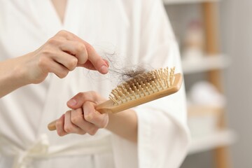Woman taking her lost hair from brush at home, closeup. Alopecia problem