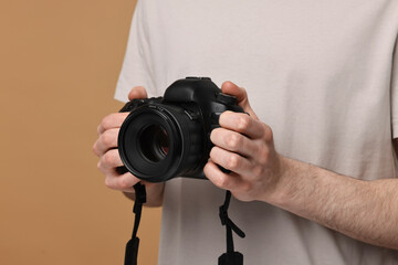 Photographer holding camera on beige background, closeup