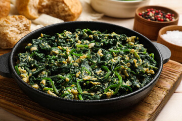 Tasty spinach dip with eggs in dish served on light wooden table, closeup