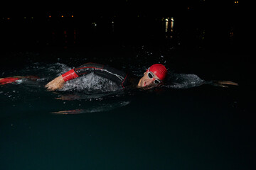 A determined professional triathlete undergoes rigorous night time training in cold waters,...
