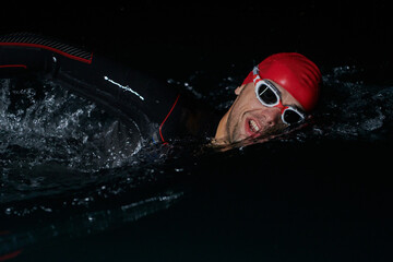 A determined professional triathlete undergoes rigorous night time training in cold waters,...