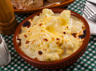Image of tasty baked cauliflower with bechamel sauce in clay pot at table