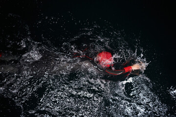 A determined professional triathlete undergoes rigorous night time training in cold waters,...