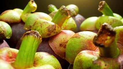 In a close-up, mangosteen fruits gleam with dark purple skin and vibrant green tops resembling...