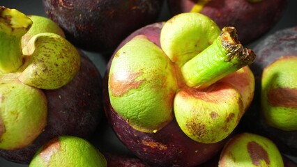 Zoom in on mangosteen fruits, showcasing their lush green caps and rich purple skins. The close-up...