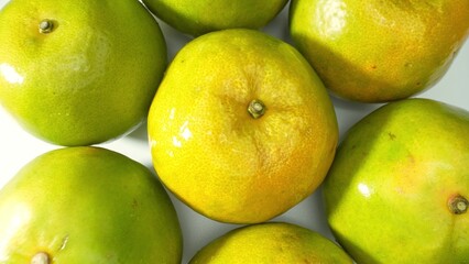 A close-up of vibrant green oranges, their glossy skins shimmering under bright light, exuding...
