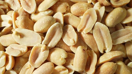Golden-brown roasted peanuts, split to unveil their savory secrets, boast a tantalizingly rough, salted surface, beckoning with warmth and flavor-a feast for the senses in every crunchy bite.
