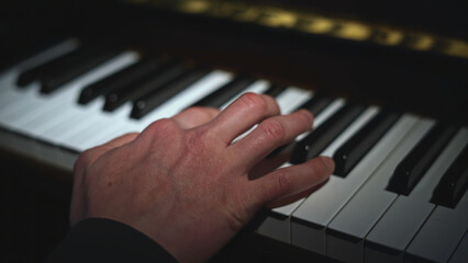 Fototapeta premium Close-up of hand playing piano. Media. Light falling on hand playing piano. Lonely hand is playing notes on piano