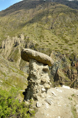 A huge stone on a thin sandstone leg on the slope of a high mountain on a sunny spring day.
