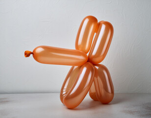 An orange balloon twisted into the shape of a playful dog against a white background