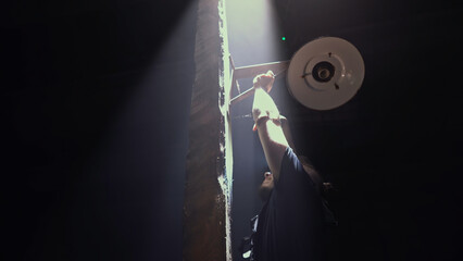 Low angle view of a male worker fixing vintage lantern on a dark background. Media. Man fixing...