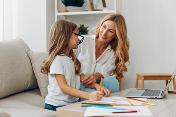 Obraz premium Mother and daughter enjoying quality time drawing and learning on the couch with a laptop and colored pencils