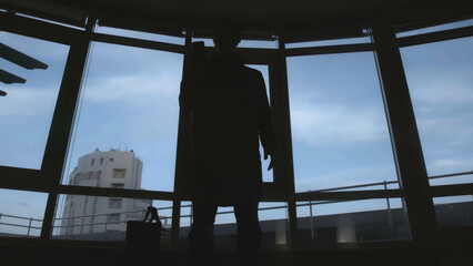 Dark silhouette of man with bag and phone. Stock. View from below of frightening silhouette of man with bag and phone. Dark shadow of man with bag pulls out phone on background of windows