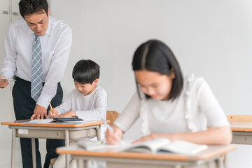 学校の教室・塾で男子生徒に勉強を教える男性教師・塾講師・先生（小学校・学童・学童保育・教育）
