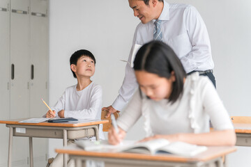 学校の教室・塾で男子生徒に勉強を教える男性教師・塾講師・先生（小学校・学童・学童保育・教育）
