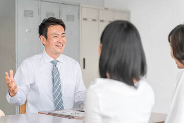 学校の教室で三者面談をする男性担任教師と女子生徒と保護者の母親
