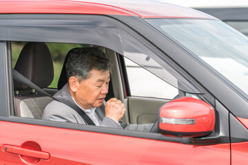運転席で咳き込む体調不良の高齢者ドライバー

