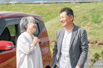 自動車の前に立っておしゃべりをする笑顔の高齢者夫婦
