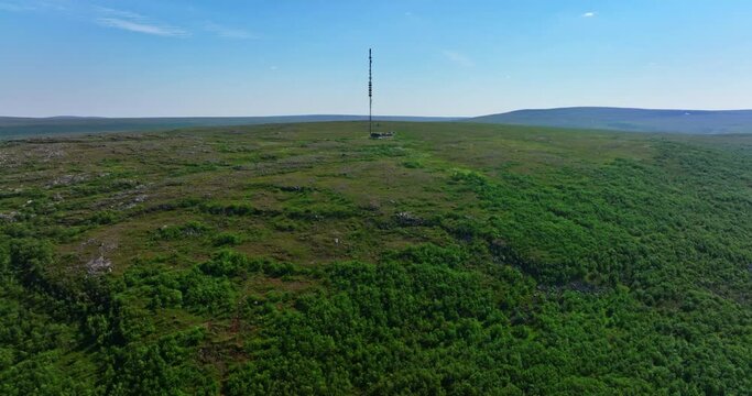 Drone rising over a fell toward a radio tower on top, summer in Utsjoki, Finland