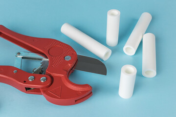 Red Pipe Cutter with White PVC Pipes on Blue Background - Plumbing Tools and Equipment