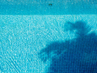 Top view space of clear water surface is rippling on swimming pool with palm tree shadow on blue...