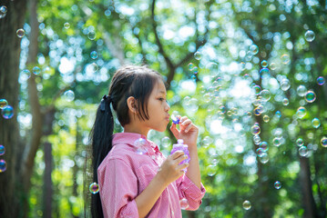 Adorable happy cute girl playful foam bubbles in green playground in summer outdoors. Funny Cheerful girl in the park with happy times.