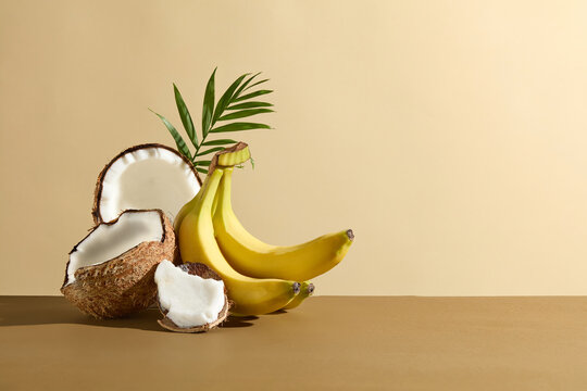The brown color flatform featuring some coconut pieces and a bunch of banana piled up on the left side, still has vacant space on the right for showing product, which extracted from fruit ingredient