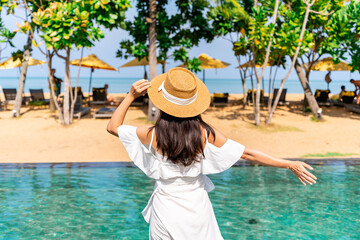 Young woman traveler relaxing and enjoying the beach view by a tropical resort pool while traveling for summer vacation, Travel lifestyle concept