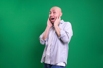 Adult Asian Bald Man Showing Shocked Expression While Standing Against Green Background
