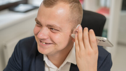 Caucasian man with a hearing aid talking on the phone on speakerphone. 