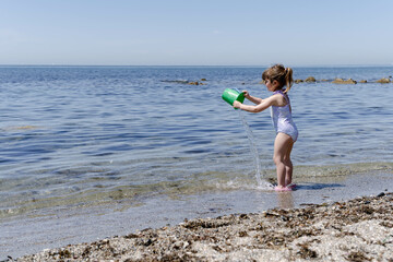 Little girl plays by pouring water with a bucket on the seashore