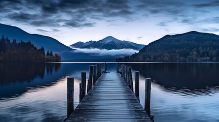 Fototapeta premium Rustic wooden pier extending into a tranquil lake at dusk, with mountains in the background