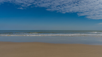 Serene minimalistic seascape. The waves of the turquoise ocean roll towards the shore, foaming and spreading over the sandy beach. Clouds in the blue sky. Copy space. Madagascar. Morondava. 