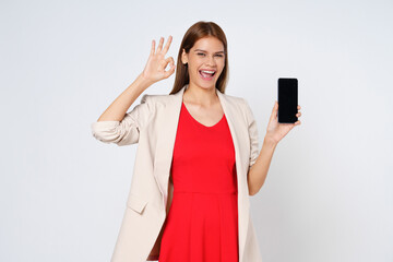 Naklejka premium Asian woman, showing smartphone screen, app interface and ok sign, recommending application on mobile phone, standing over white background.
