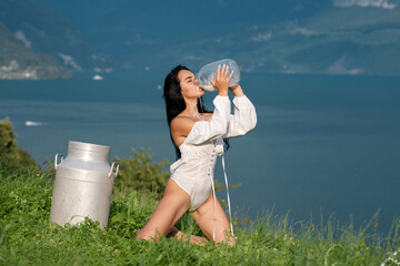 Woman drink milk at Swiss Alps in Switzerland. Young woman drinking milk from bottle. Milking day. Sexy milky mouth with splash. Model drink Milk at Alpine meadow. Woman body with face splashed milk.